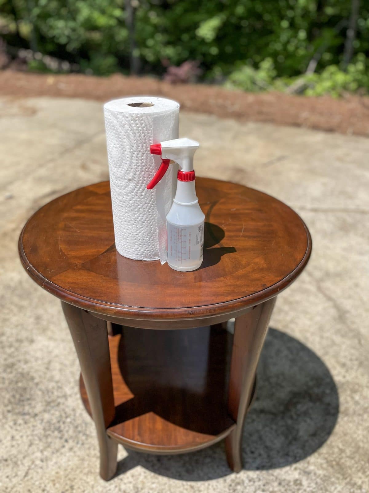 round cherry end table sitting in drive with bottle and paper towels